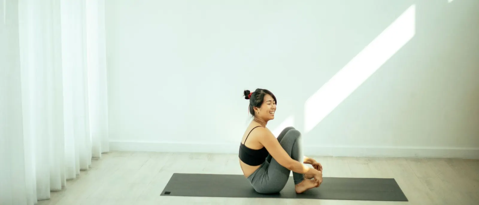 A woman sitting quietly on a yoga mat in a bright, empty studio